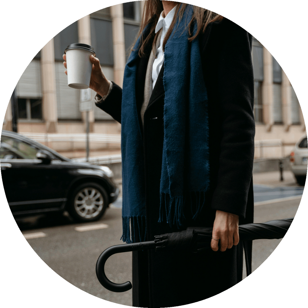 Woman in busy city street with coffee and umbrella